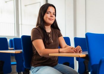 Jeune femme brune assise dans une salle de classe regarde la caméra