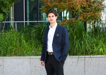 Jeune homme brun en costume dehors face à la caméra
