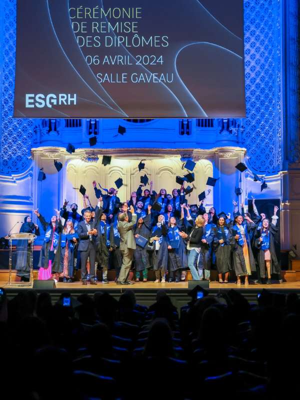 Etudiants diplômés habillés en noir sur une scène heureux jettent leurs chapeaux