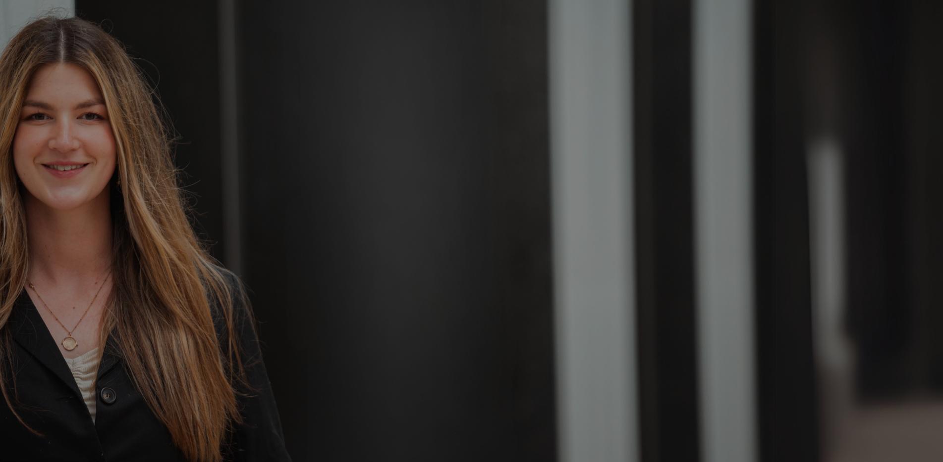 Femme souriant à la caméra en tenue professionnelle avec une veste grise et les cheveux long ESGRH